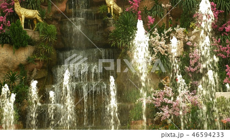a large artificial waterfall framed by pink flowers and green leaves. 46594233