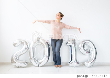 New 2019 Year is coming. Cheerful young woman standing near silver colored numbers in white room New 2019 Year is coming. Cheerful young woman standing near silver colored numbers in white room 46596712