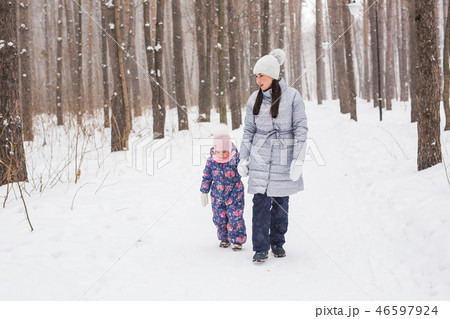 Winter, family and people concept - mother is walking with her daughter in winter forest. 46597924