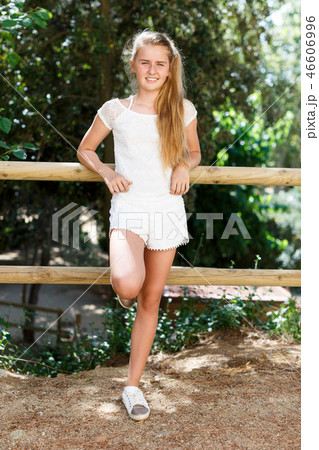 Teenage cute girl standing near fence in green park at sunny day Teenage cute girl standing near fence in green park at sunny day 46606996