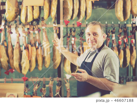 Smiling mature man seller working with tasty jamon Smiling mature man seller working with tasty jamon 46607188