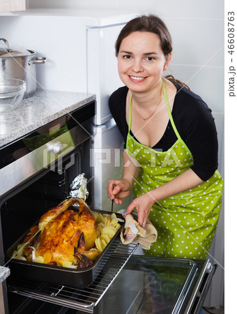 Smiling positive woman roasting cockerel for dinner Smiling positive woman roasting cockerel for dinner 46608763