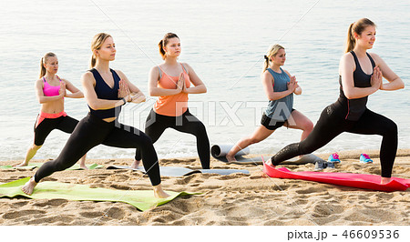 Positive women standing on yoga asana on beach Positive women standing on yoga asana on beach 46609536