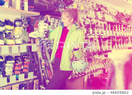Customer woman in jacket and helmet is choosing boots for skiing Customer woman in jacket and helmet is choosing boots for skiing 46609862