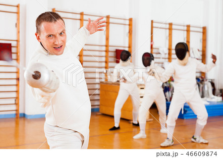 Sporty young man fencer practicing effective fencing techniques in training room Sporty young man fencer practicing effective fencing techniques in training room 46609874