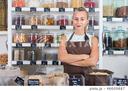 Portrait of girl seller who is standing near showcase with nuts 46609887
