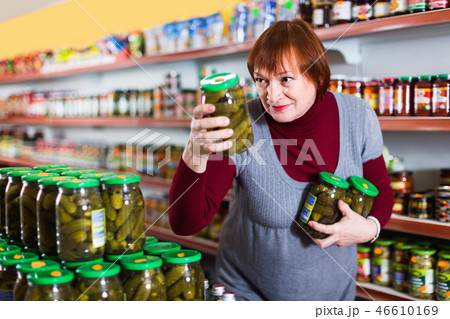 Adult female customer holding glass jar of cucumbers in the supermarket 46610169