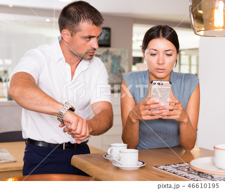 Annoyed man pointing at watch to girlfriend with phone Annoyed man pointing at watch to girlfriend with phone 46610195
