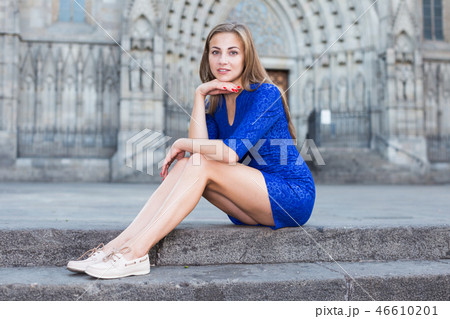 Cheerful female is playfully posing sitting in blue dress on the stairs 46610201
