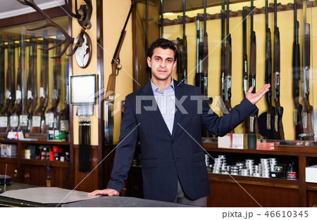 Handsome adult male owner of hunting shop offering rifle 46610345