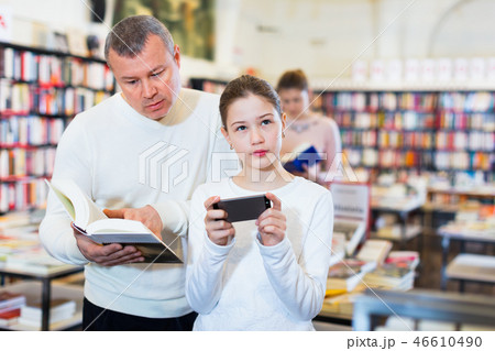 Father trying to draw daughter attention to book while she carried away with phone 46610490