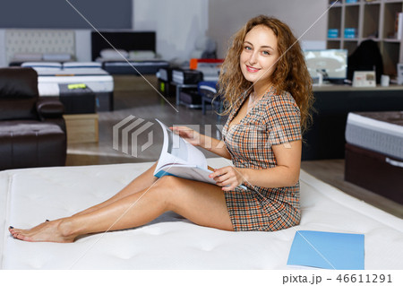 Young attractive woman choosing right mattress with booklet in home furnishings store 46611291