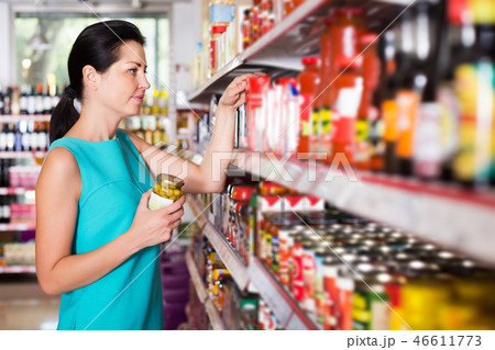 female in the shop holding preserved jar of olives 46611773