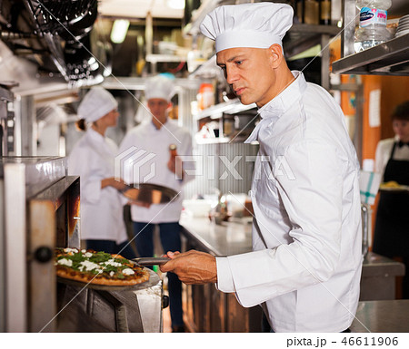 Confident chef getting pizza out of oven Confident chef getting pizza out of oven 46611906