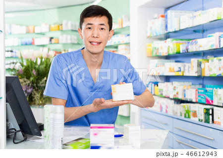 Portrait of chinese man pharmacist who is standing on his work place near cashbox in apothecary. 46612943