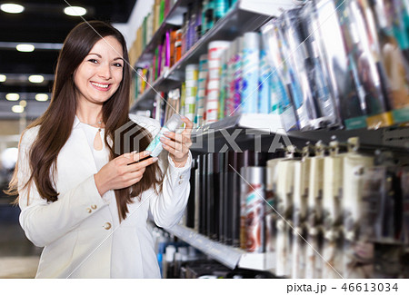 Smiling young female choosing haircare spray and other products at the shop 46613034