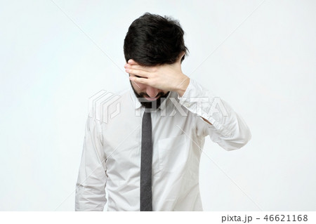 Exhausted young man covering face with hand while standing against grey background 46621168