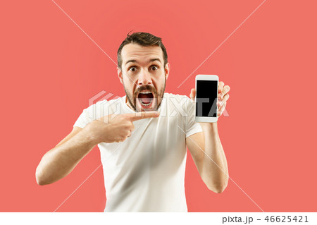 Young handsome man showing smartphone screen isolated on coral background in shock with a surprise 46625421