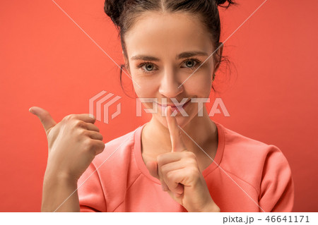 The young woman whispering a secret behind her hand over coral background The young woman whispering a secret behind her hand over coral background 46641171