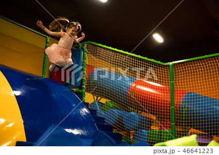 Little girl is jumping in the dry pool with bright soft cubes for play in kids play room Little girl is jumping in the dry pool with bright soft cubes for play in kids play room 46641223