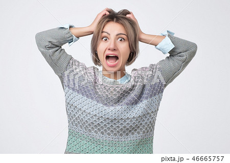 Shocked amazed young woman with hands on head standing and shouting Shocked amazed young woman with hands on head standing and shouting 46665757