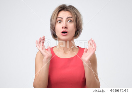 Surprised shocked female wearing red dress, keeping her hand up, opening mouth. 46667145