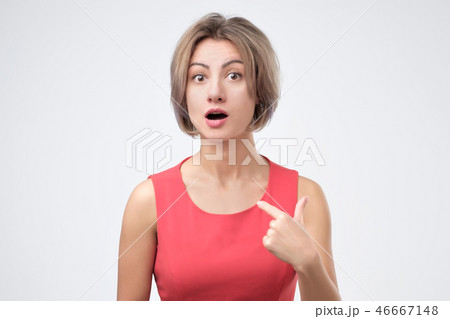 Pretty young woman in red dress pointing at herself in excitement being puzzled with success 46667148