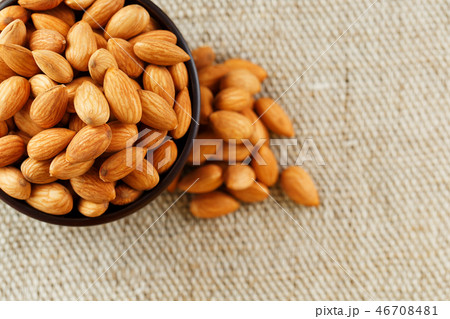 Almonds in a wooden cup on a burlap cloth background. Almonds in a wooden cup on a burlap cloth background. 46708481