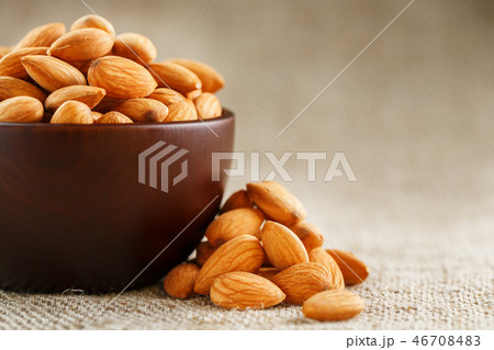Almonds in a wooden cup on a burlap cloth background. Almonds in a wooden cup on a burlap cloth background. 46708483