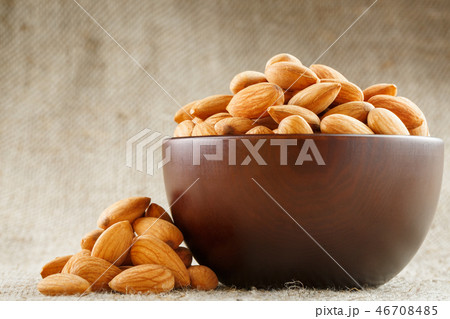 Almonds in a wooden cup on a burlap cloth background. Almonds in a wooden cup on a burlap cloth background. 46708485