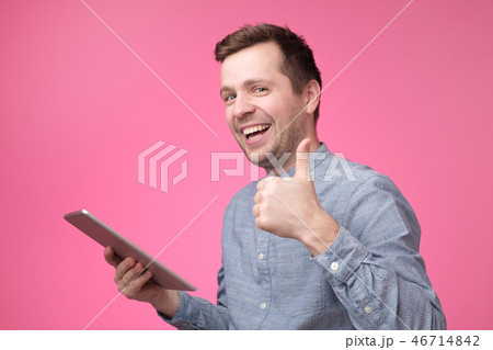 Man holding tablet raising thumbs up and smiling broadly, giving positive feedback 46714842