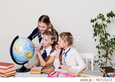 three girls schoolgirls on the lesson of geography with a globe in school 46715213
