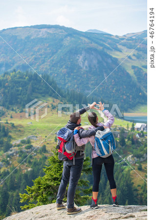 Two hikers at viewpoint in the mountains enjoying beautiful view of the valley with a lake. 46764194