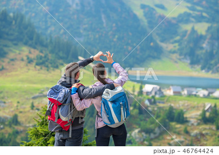 Two hikers at viewpoint in the mountains enjoying beautiful view of the valley with a lake. Two hikers at viewpoint in the mountains enjoying beautiful view of the valley with a lake. 46764424