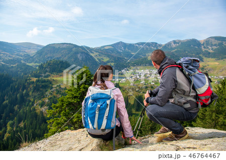 Two hikers at viewpoint in the mountains enjoying beautiful view of the valley with a lake. 46764467