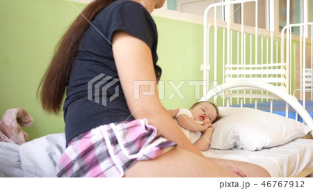 child sleeps in the hospital ward on white bed under the supervision of mom. mother measures 46767912
