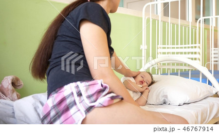 child sleeps in the hospital ward on white bed under the supervision of mom. mother measures 46767914