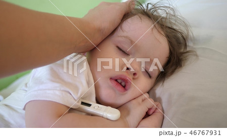 mom measures temperature with thermometer to baby and caresses child with hand. close-up. baby mom measures temperature with thermometer to baby and caresses child with hand. close-up. baby 46767931
