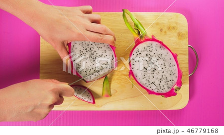 top view, female hand cuts the fruit with a knife on a wooden board, white dragon fruit. The concept 46779168