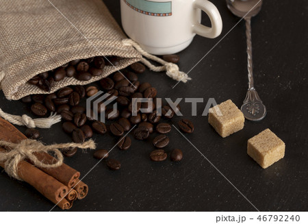 burlap with roasted coffee beans, cane sugar, coffee cup on stone surface 46792240