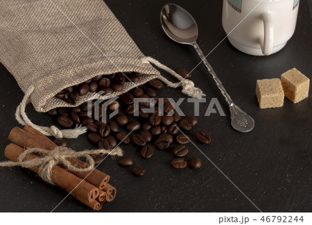 burlap with roasted coffee beans, cane sugar, coffee cup on stone surface 46792244