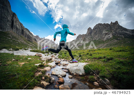 Woman trail runner jumping over small river Woman trail runner jumping over small river 46794925