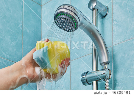 Wet sponge in human hand under shower head 46809491