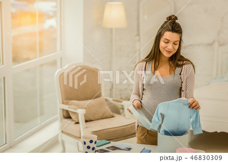 Smiling pregnant woman unpacking new children clothes Smiling pregnant woman unpacking new children clothes 46830309