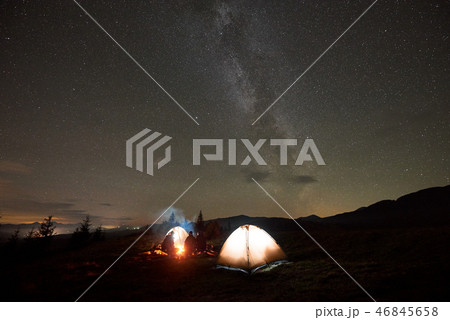 Group of tourists with guitar by burning bonfire under dark starry sky with Milky Way constellation. 46845658