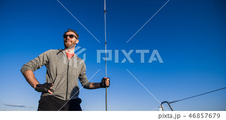 Young man wearing sunglasses standing on yacht stern and enjoying perfect autumn day under sails - 46857679