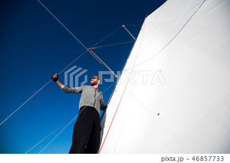 Yacht captain with a beard stands on sail boom on a sailing yacht, holding the rope in his hand and Yacht captain with a beard stands on sail boom on a sailing yacht, holding the rope in his hand and 46857733