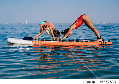 Mom and little daughter doing yoga on the paddle board Mom and little daughter doing yoga on the paddle board 46857833