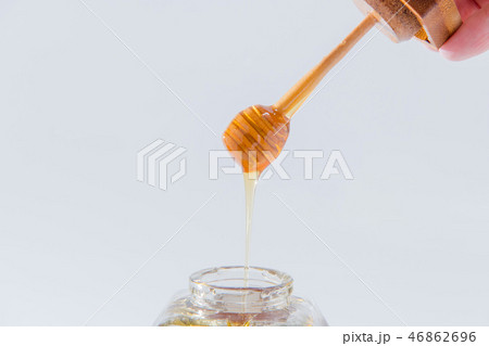 ハニーは、白い背景の上に木製蜂蜜ディッパーから滴ります 46862696