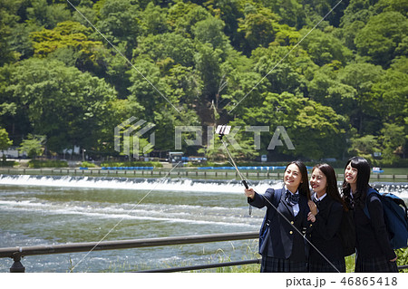川を背景に自撮り棒で自撮りする二人の女子高生 46865418